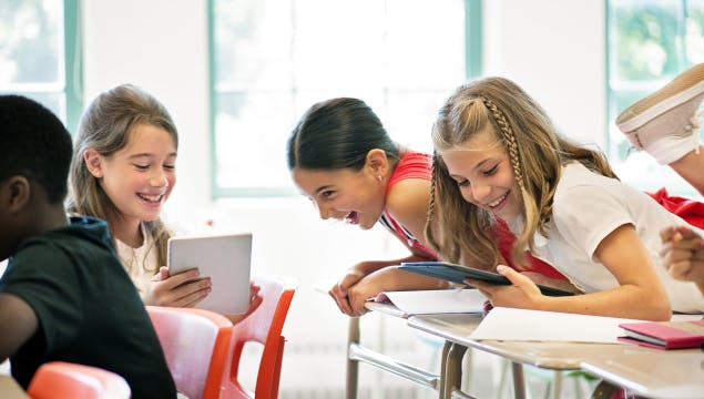 A group of elementary students laughing in class and using tablets.