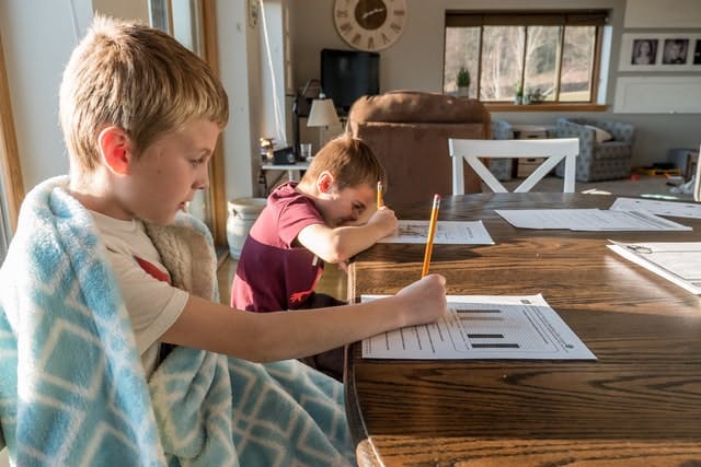 Two siblings doing homework at the dinner table.