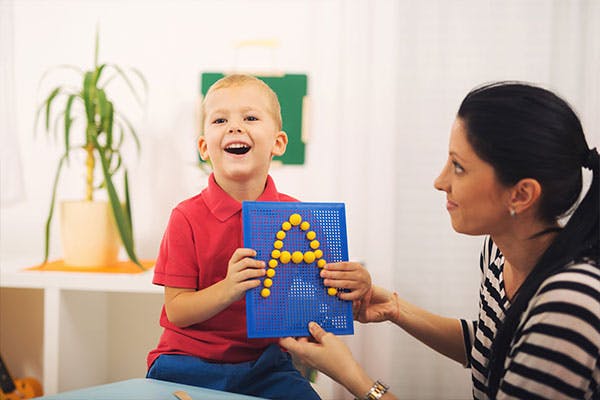 An educator working with a young student on his letters.