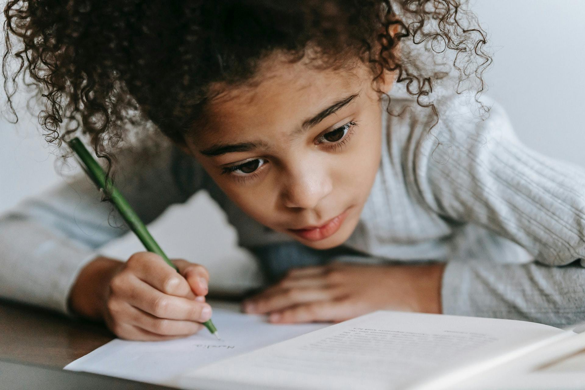 A young girl practices writing a story with a paper and pencil. 