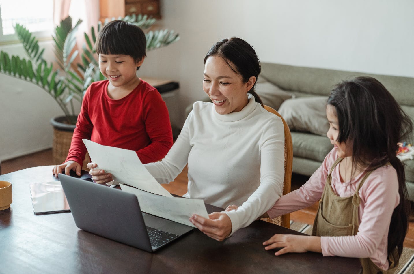 Mom at her computer with her two kids beside her, smiling at pictures they drew.