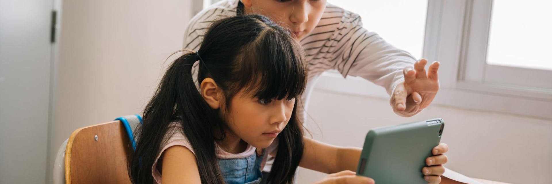 Two students play on a tablet with one of the many learning apps for kids.