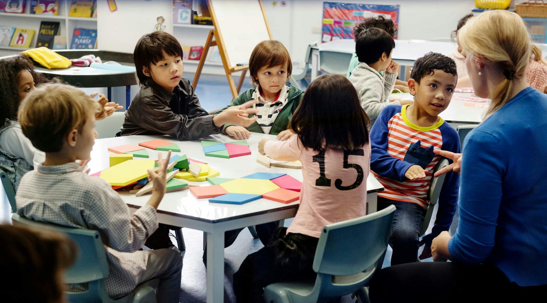 Students sit around table with teacher.