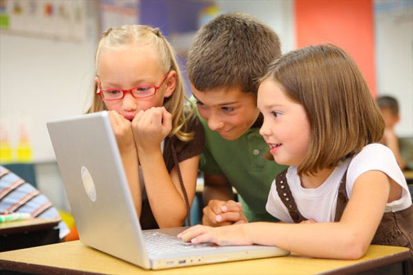Elementary students gather around a laptop during class.