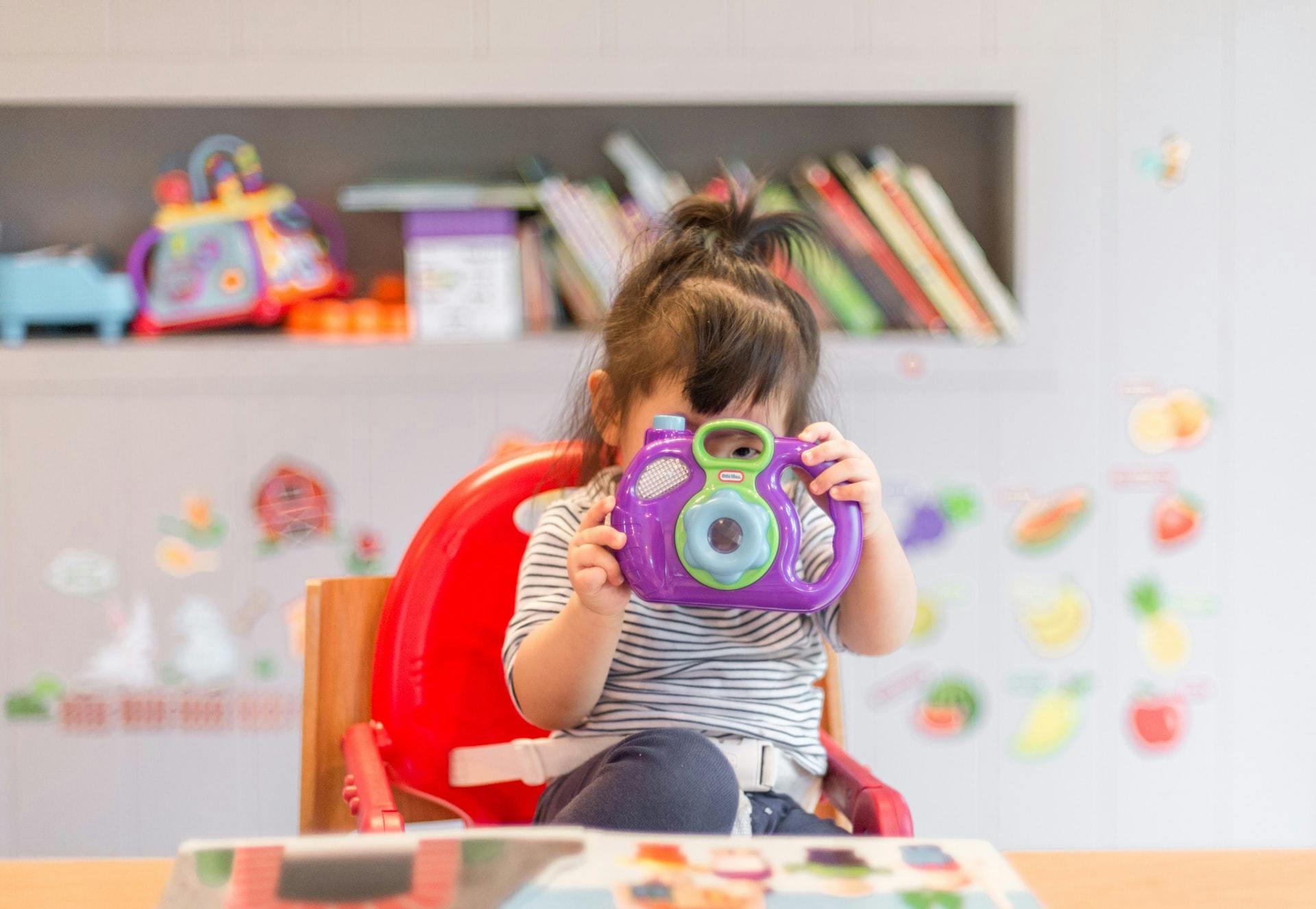 A young child plays with a toy camera in a classroom using play-based learning activities.