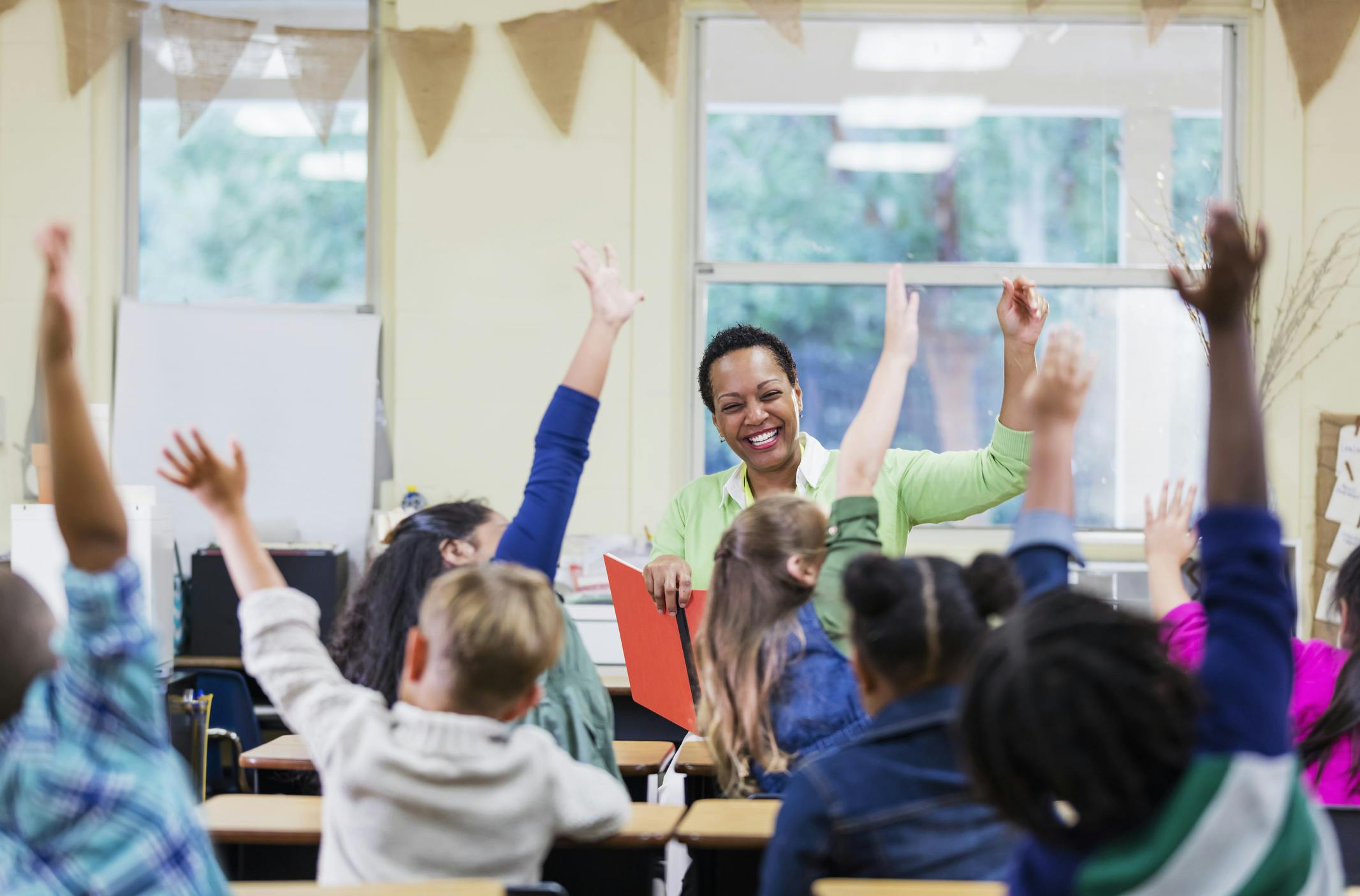 Teacher sitting in front of her class of students with their arms raised