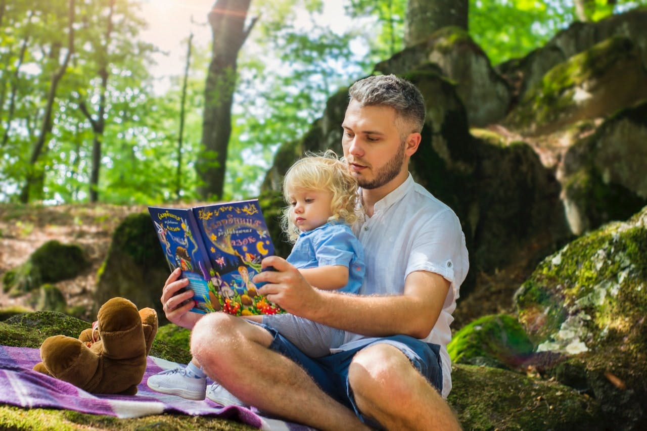 Father and daughter read together in the woods during a summer reading program. 