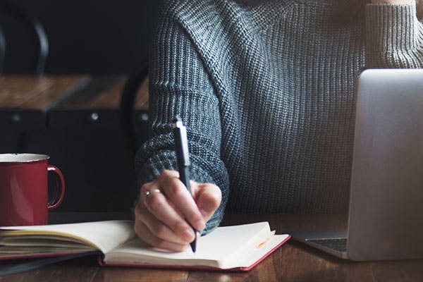 Teacher at desk writing with paper and pen.