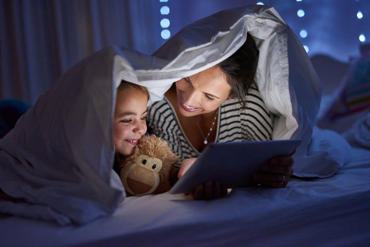 Child and her mother using a reading app in a blanket fort