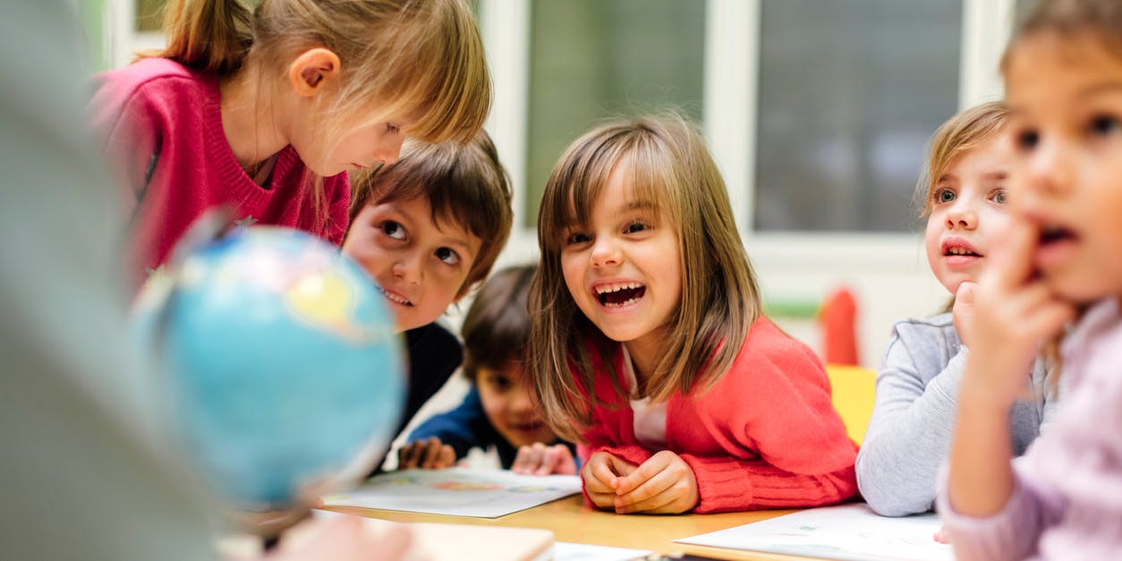 A group of primary students sitting and standing around a desk having an exciting conversation.