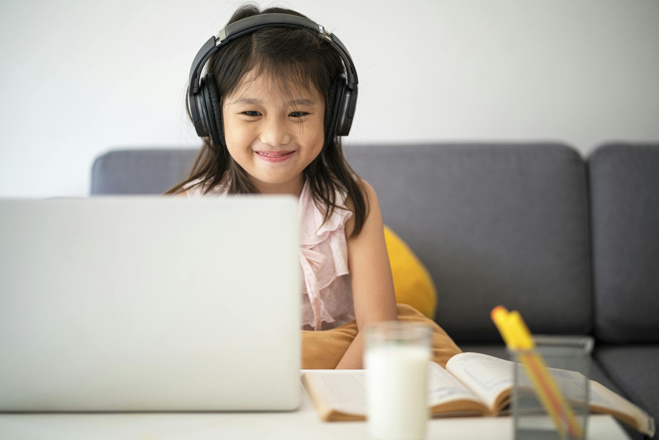 child sitting on couch with headphones on, smiling and learning on a laptop. 