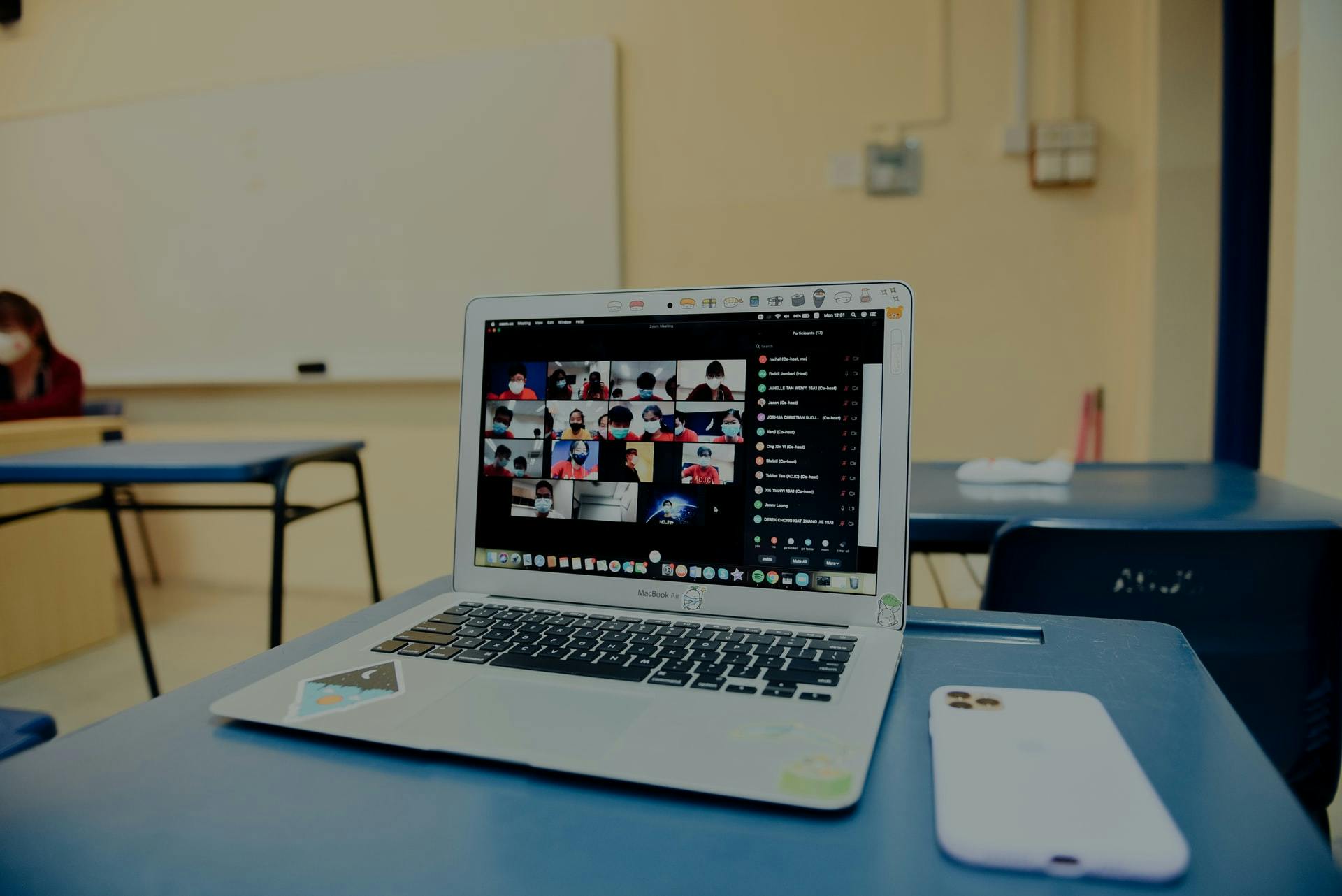 Computer with zoom classroom on the screen sits on a desk in a classroom. 