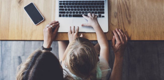 Daughter sits with mother using laptop.