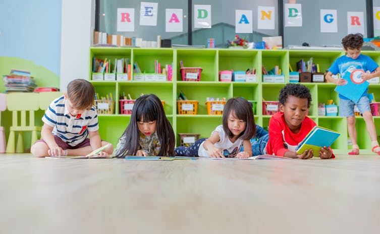 Students reading books in class with book bins for classroom library in the background.