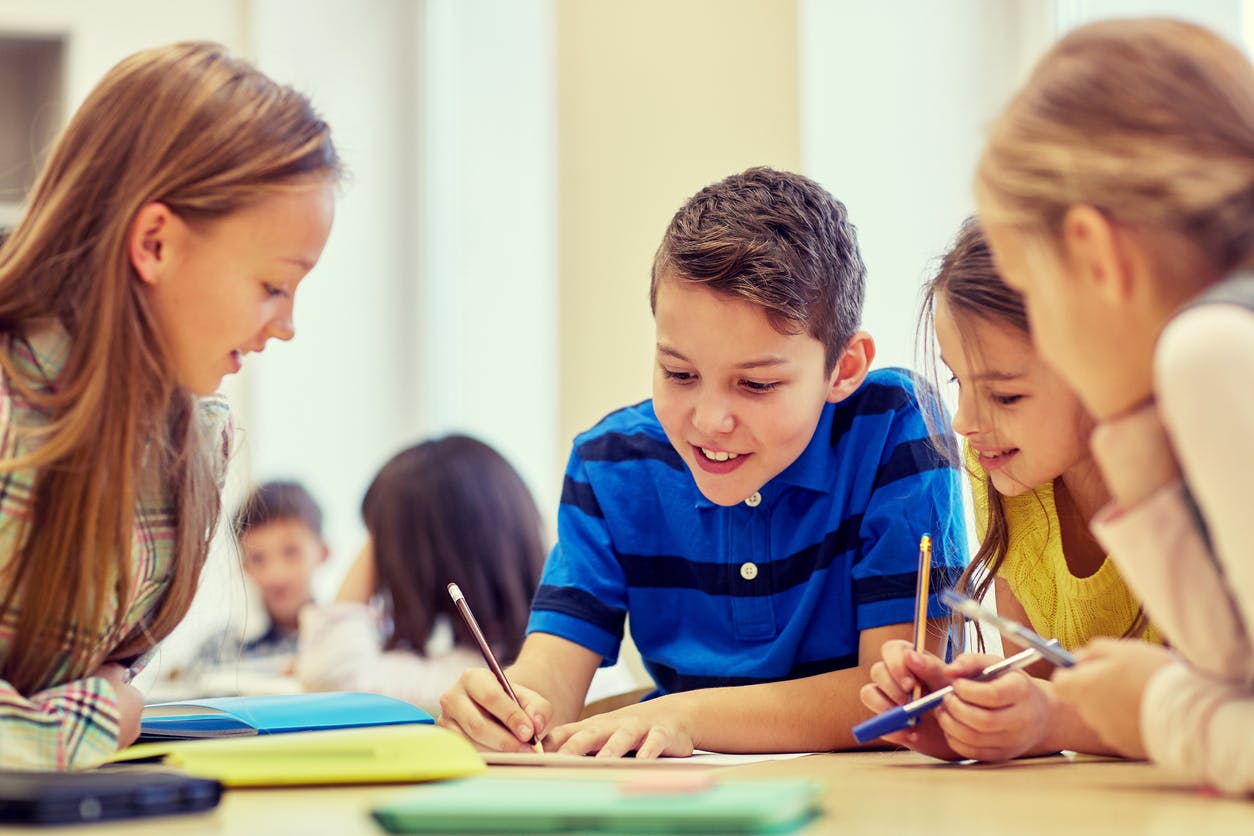 Elementary kids gathered around a table talking and writing during a student-centered learning activity.