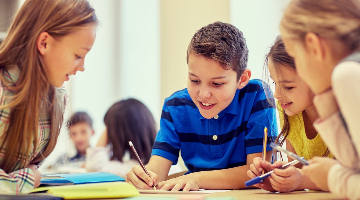 Elementary kids gathered around a table talking and writing during a student-centered learning activity.