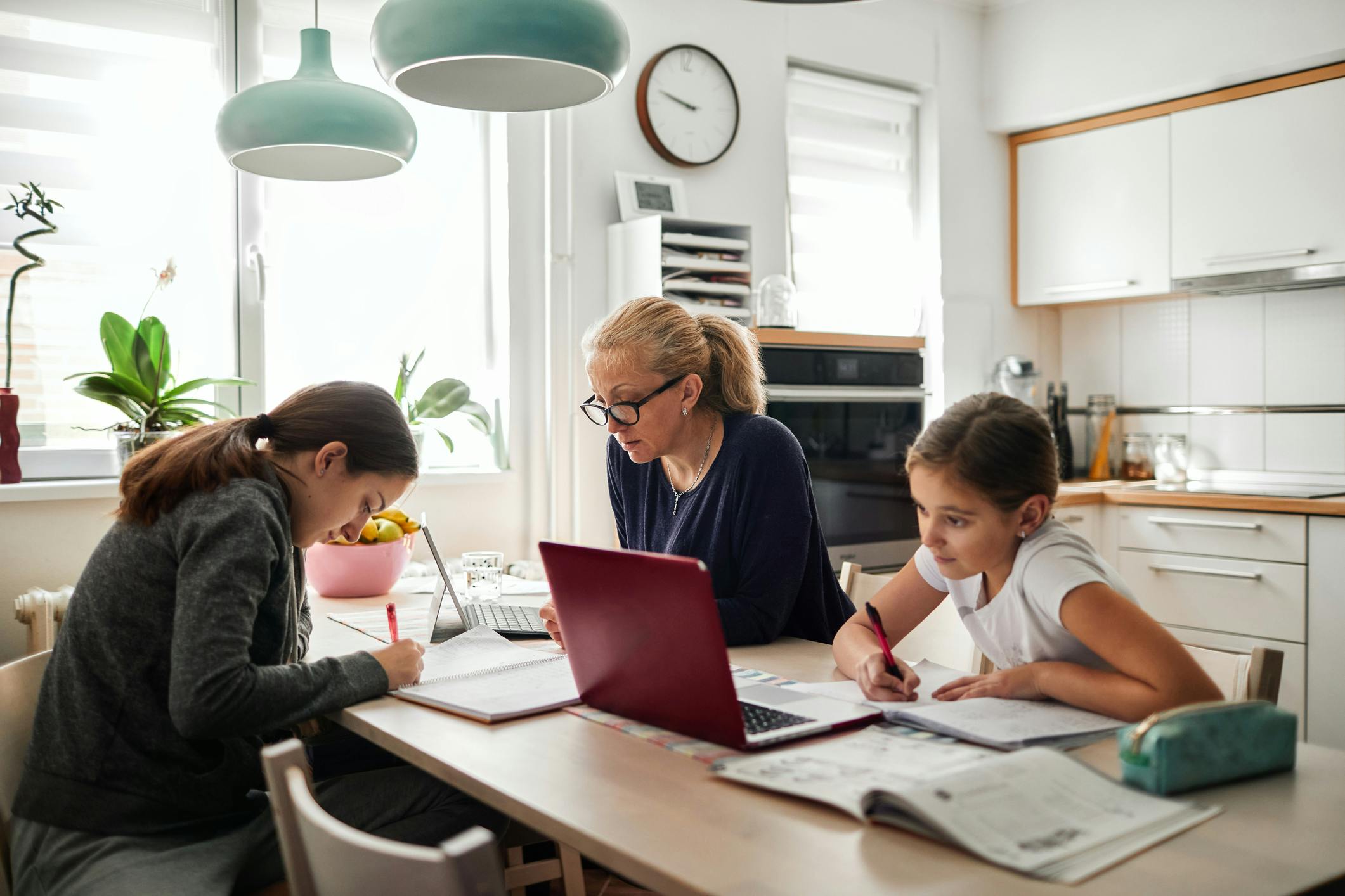 Mother and her two daughters working at the kitchen table together.