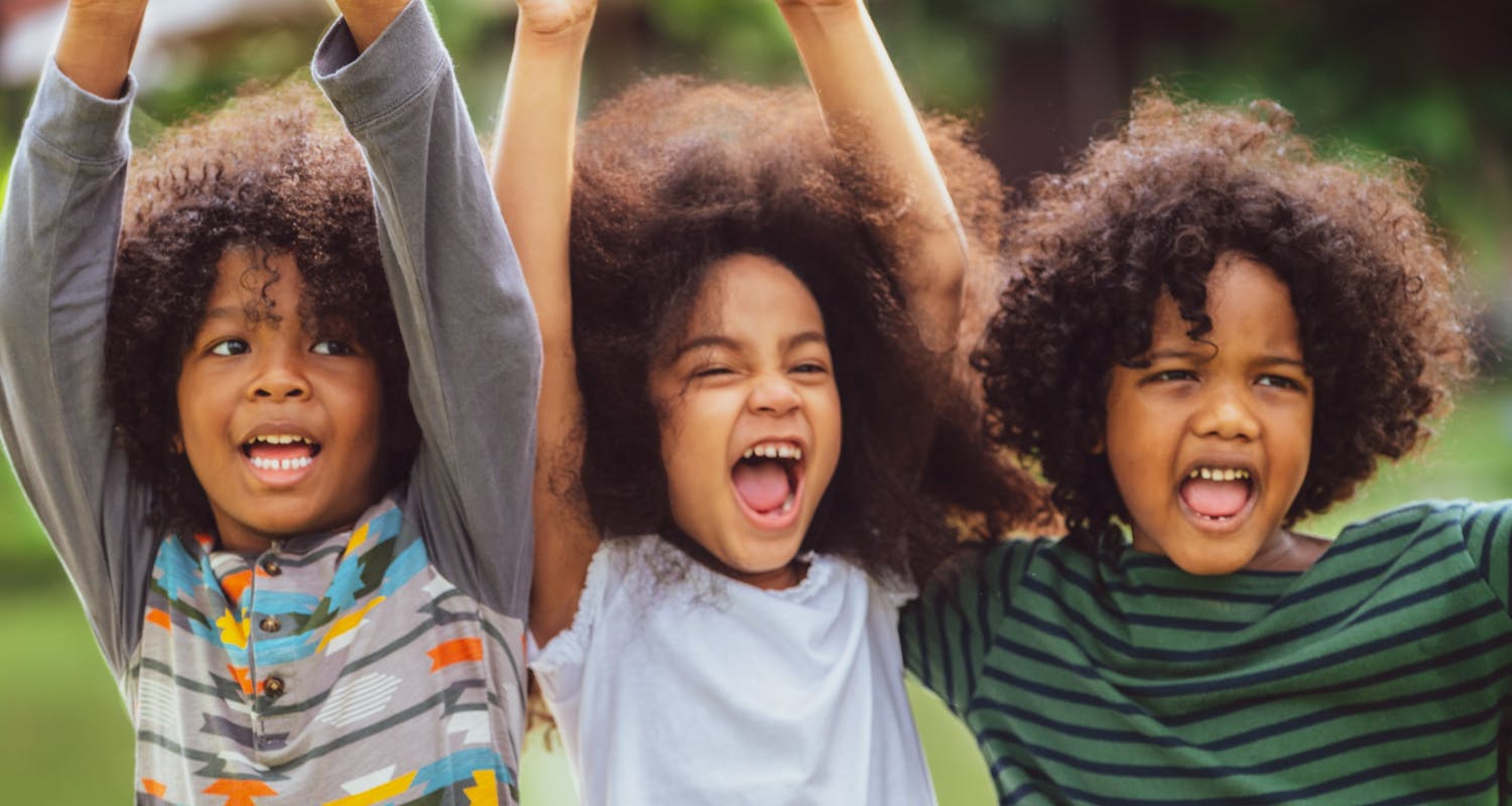 Excited trio of kids with hands up in the air, smiling and having fun together.