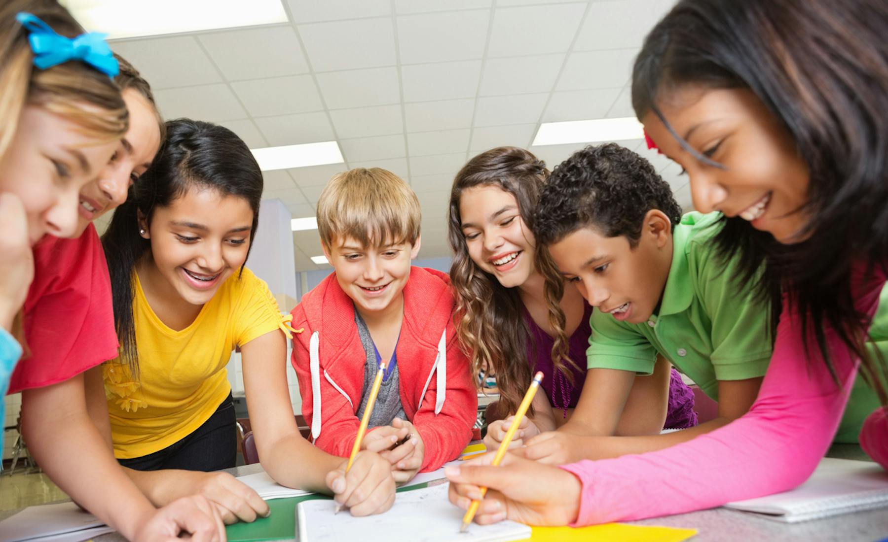Seven middle school students gather around a table smiling while doing a writing exercise.