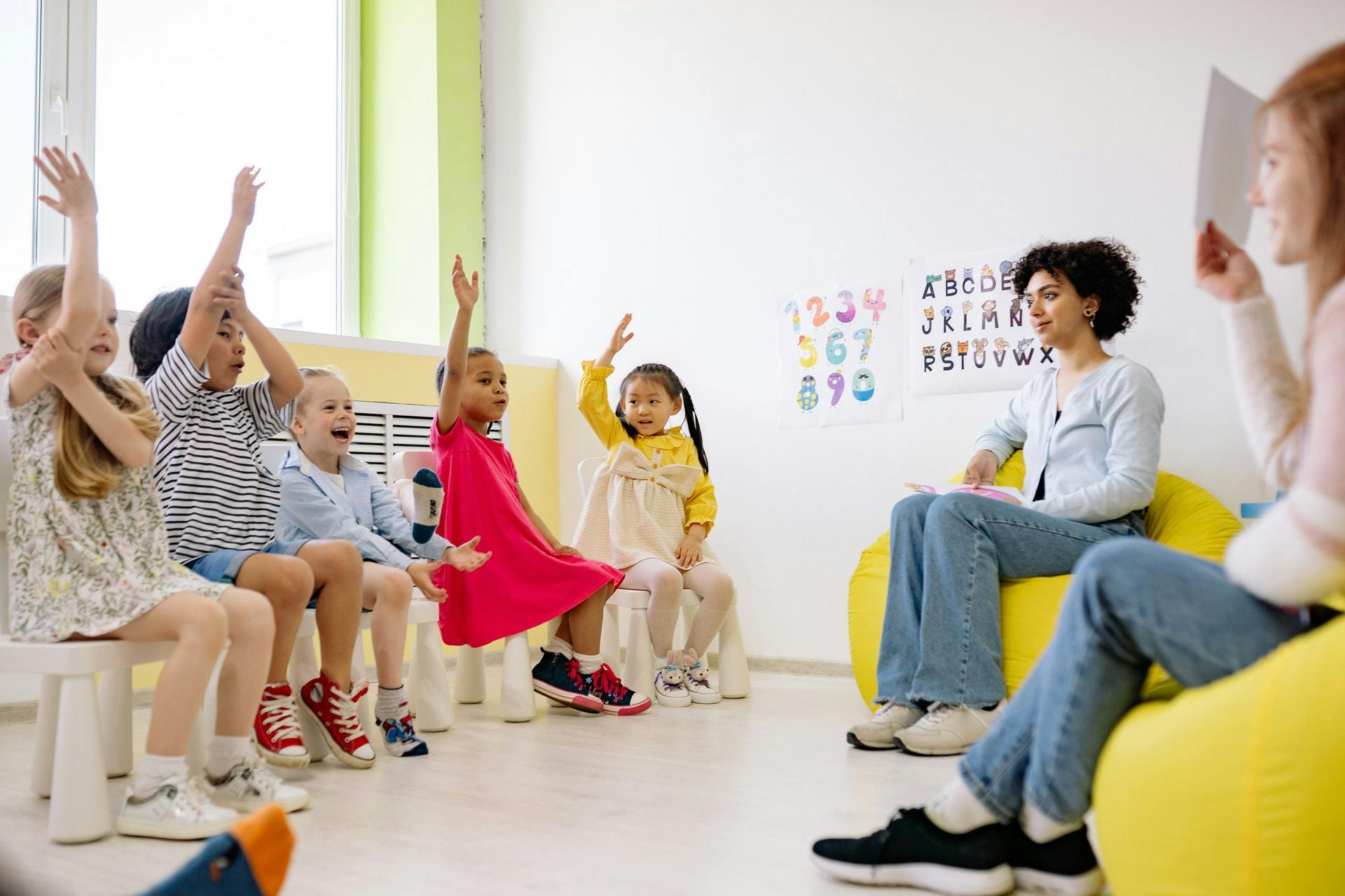 A group of students sits on stools in the classroom and raise their hands during restorative justice activities. 