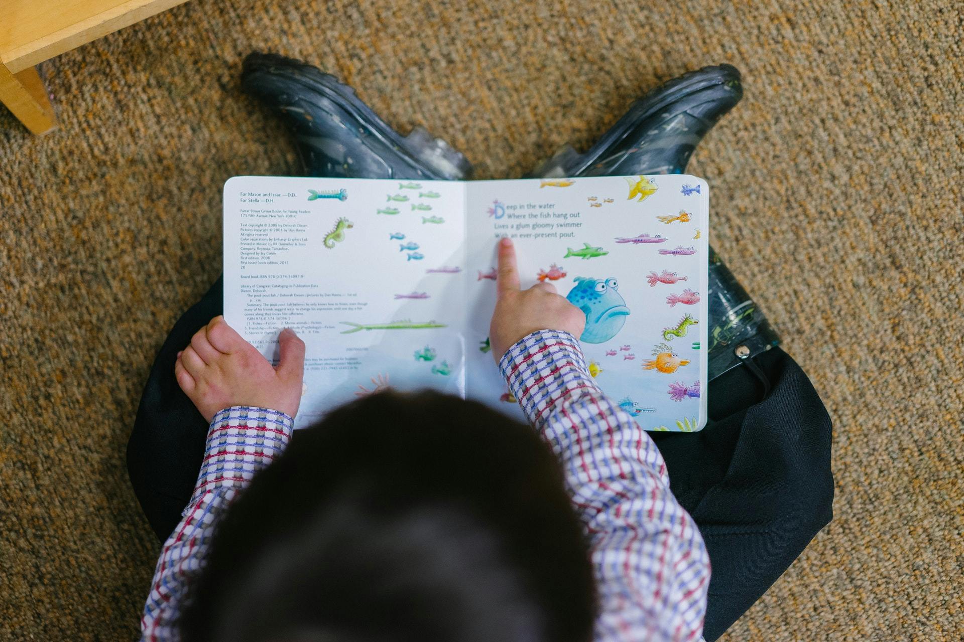 A student points at words in a picture book as they practice reading comprehension skills.