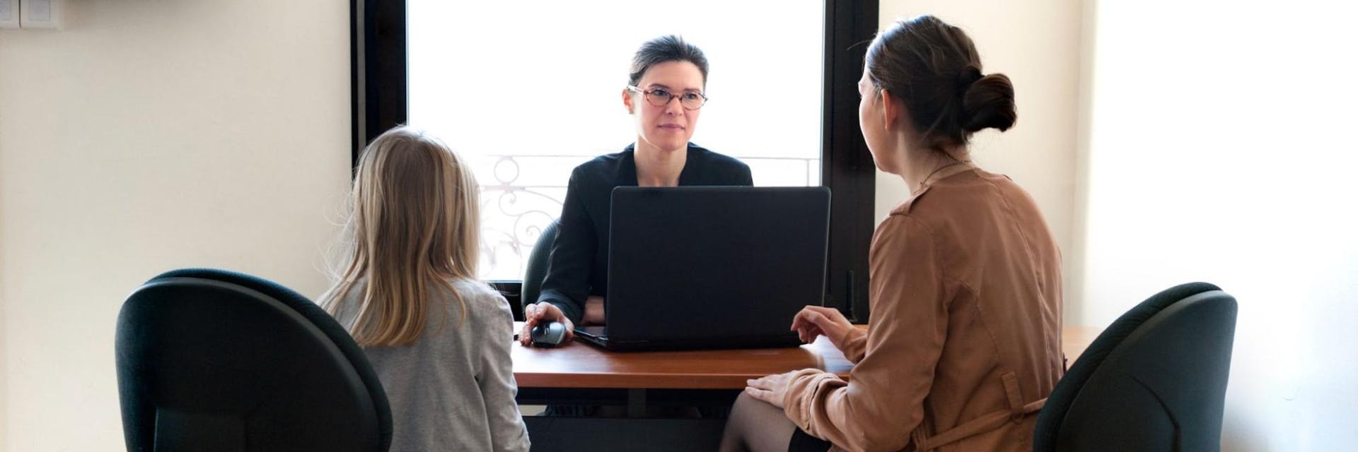 Parent and daughter sit opposite a teacher during a parent teacher conference.