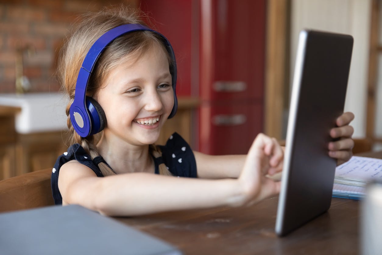 Excited child wearing headphones, enjoying a Prodigy Ultimate Membership on her tablet.