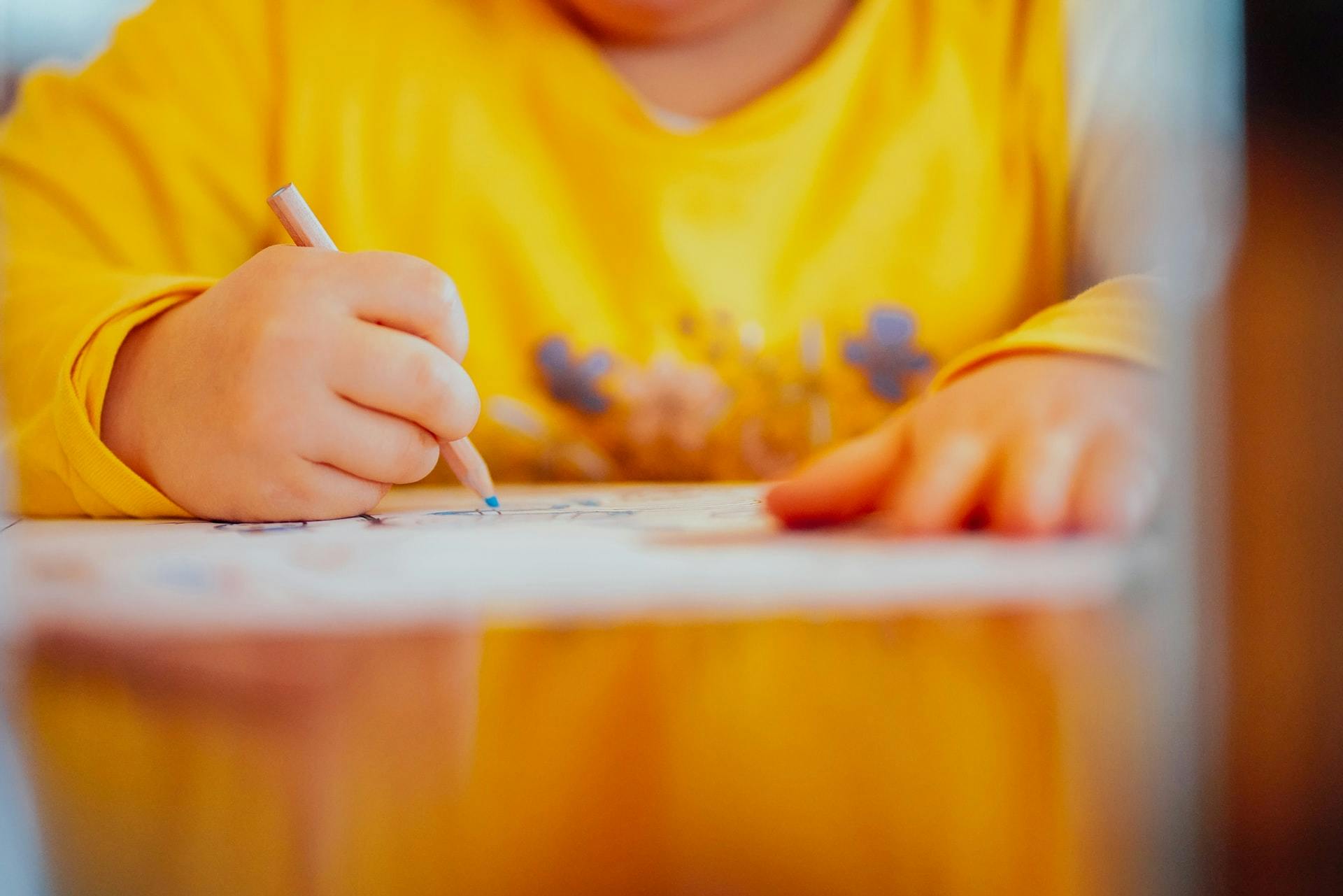 Young student sits at a table with pencil and paper during creative writing activities. 