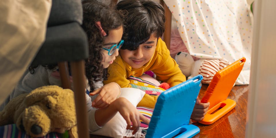 Two happy, focused children playing Prodigy on their tablet computers together.