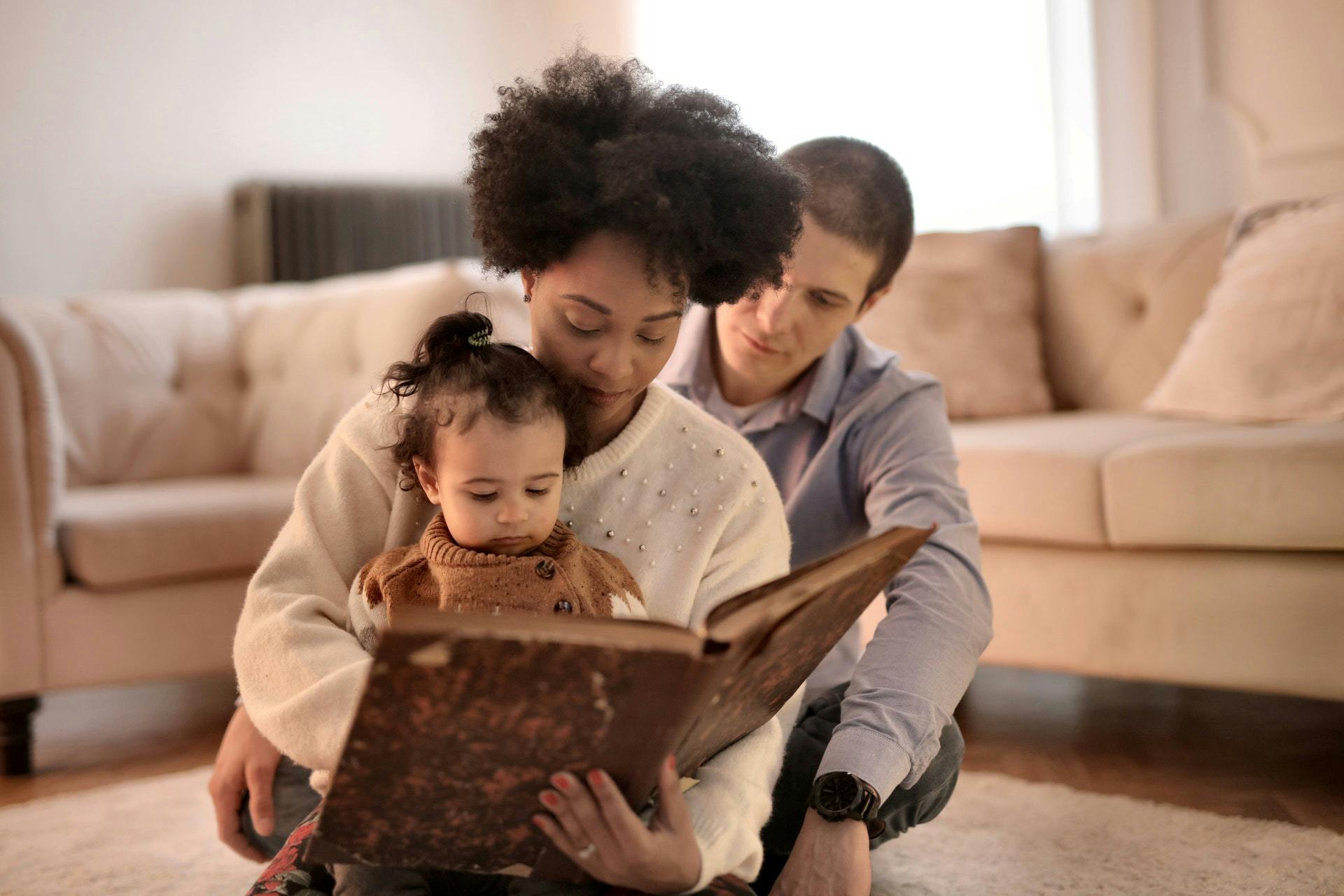 A family sits on the ground together and reads a book. 