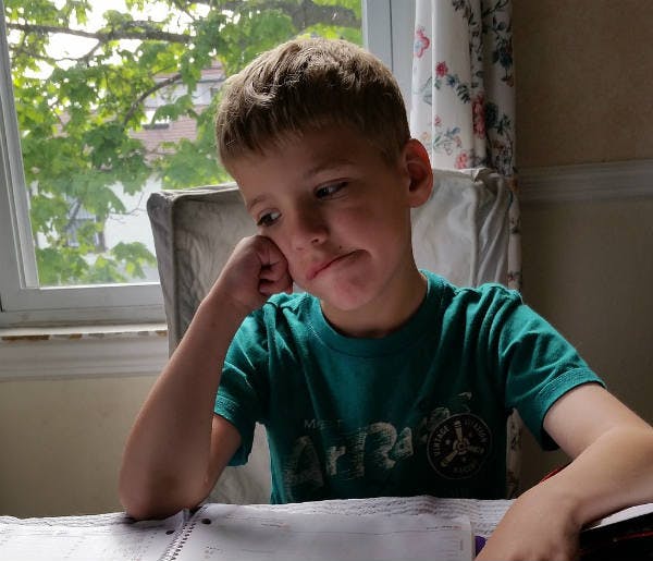 A boy is sitting besides a window with a confusing face