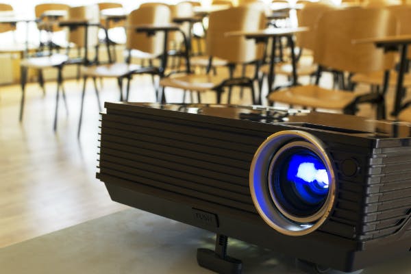 A projector in front of rows of classroom chairs.