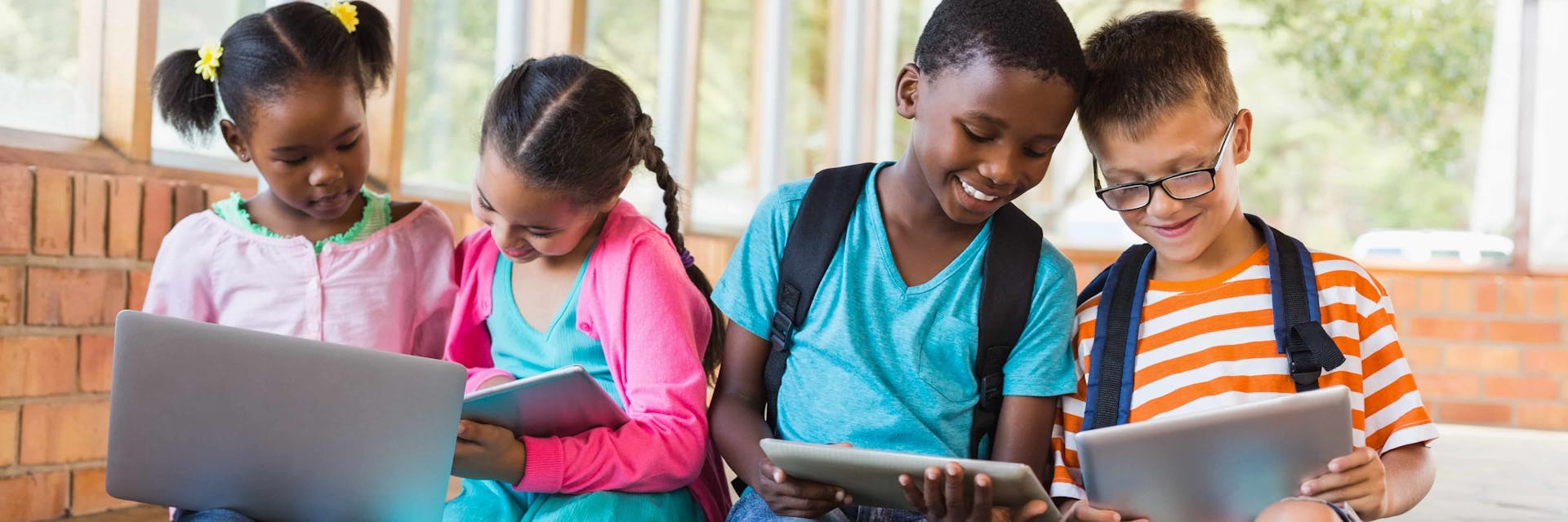 Four kids playing long division games on laptops and tablets.