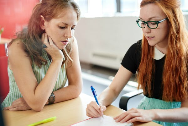 Two teachers are discussing math with a pen and a notebook