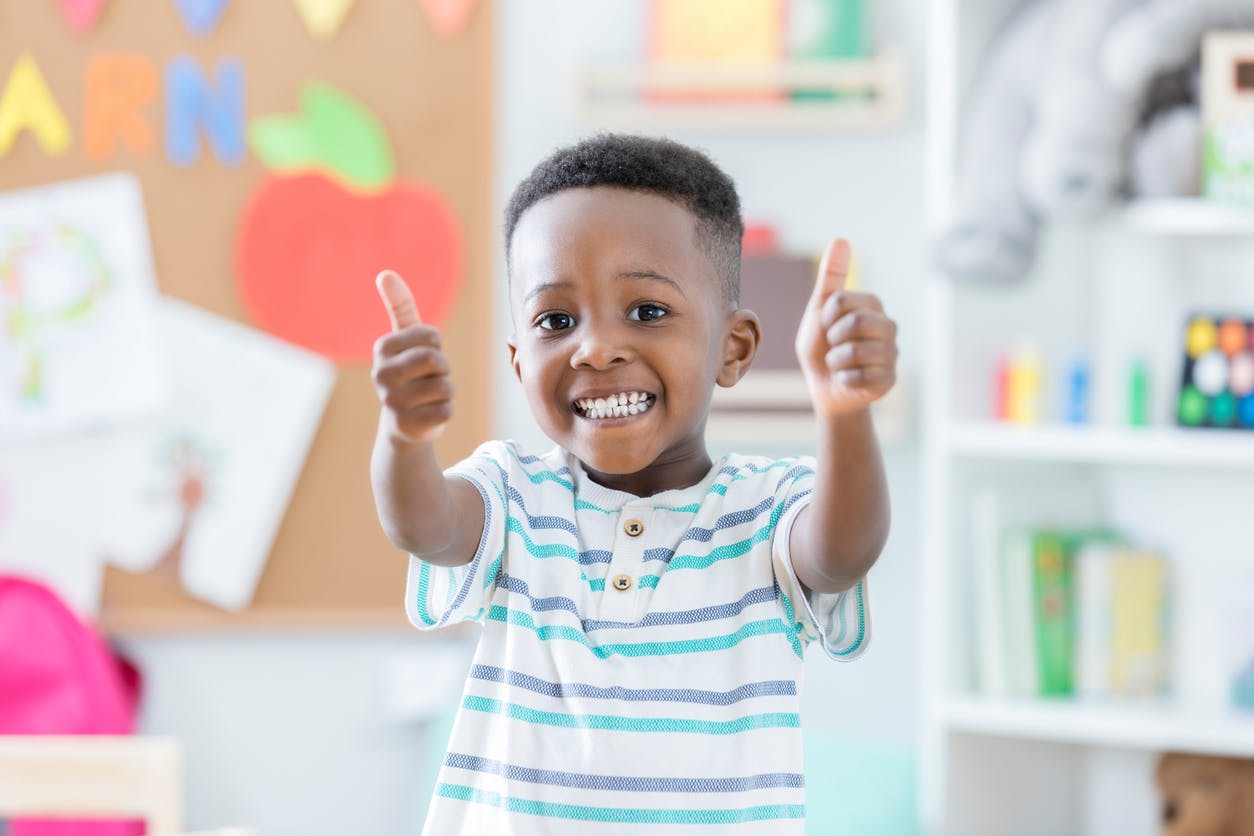 Confident child gives two thumbs up at school, after achieving his educational goals.