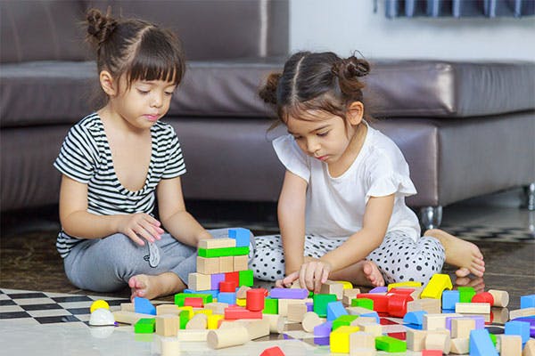 Two young children are sitting on the ground and building block