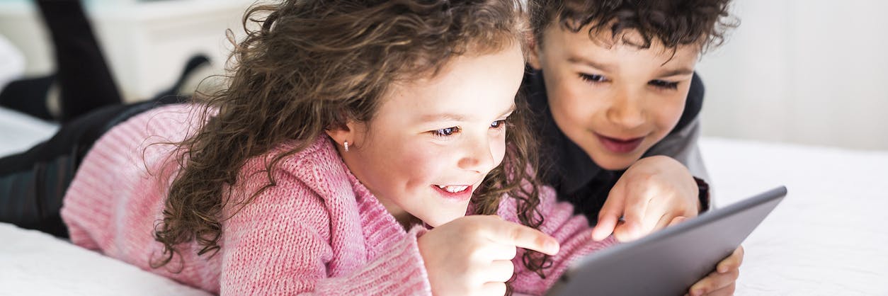 Two kids smiling while using Prodigy on their tablet.