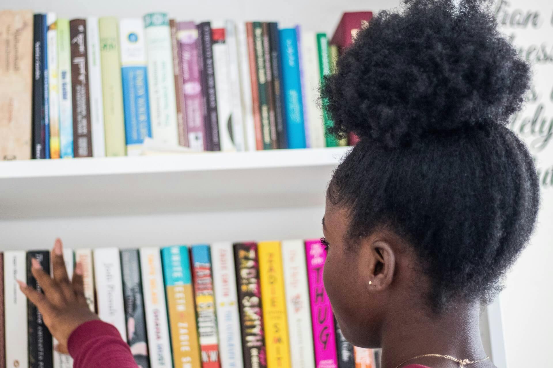 A girl picking a book off of her bookshelf.