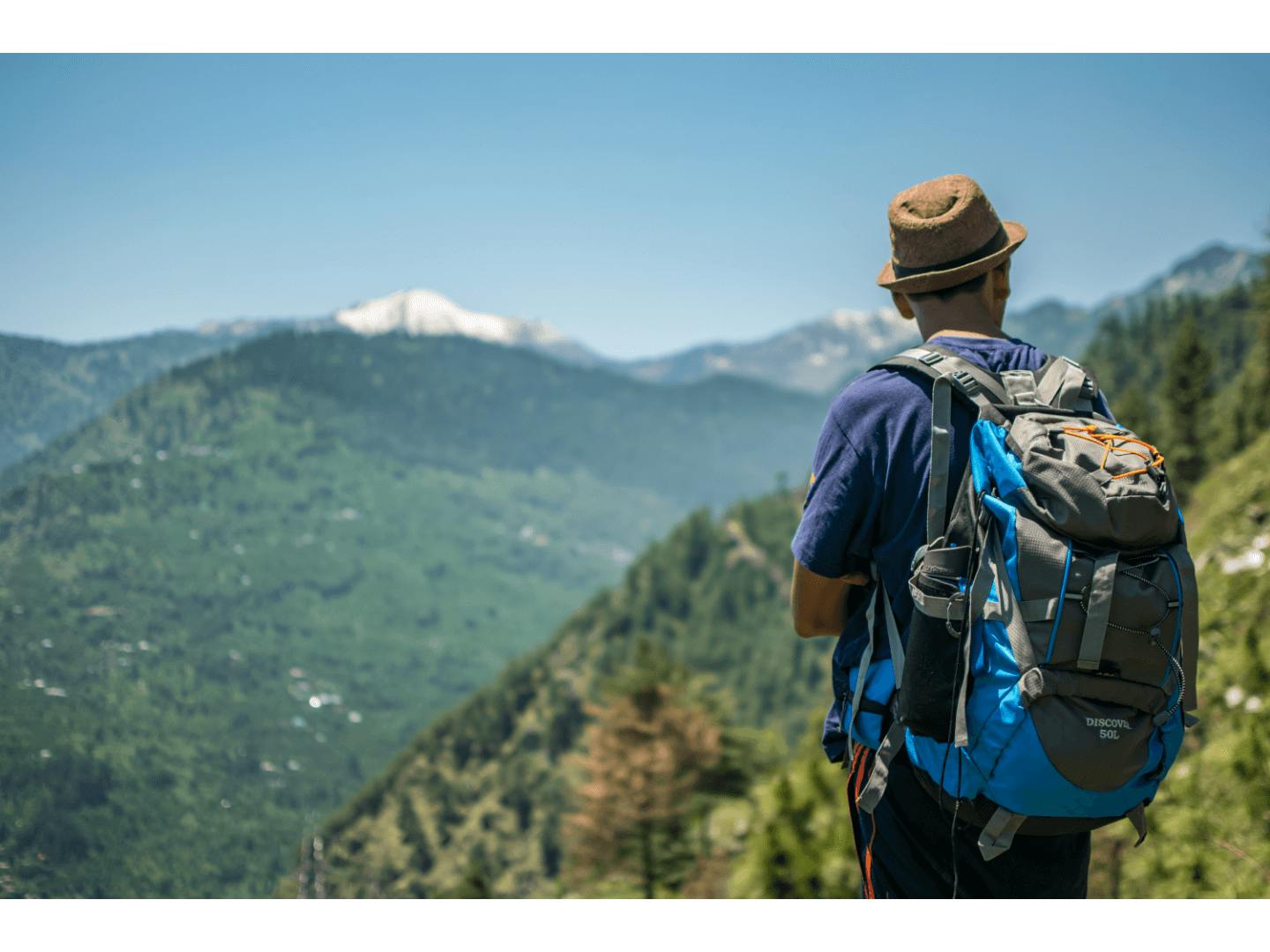 A man on a hike facing away from the camera, with a mountain view in the background