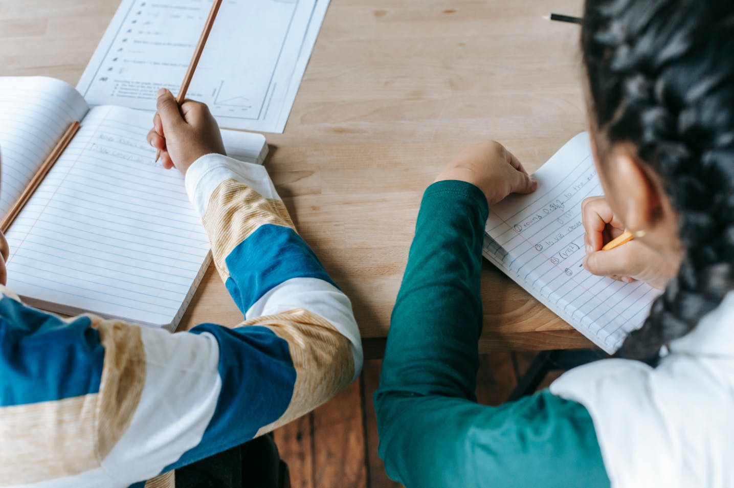 Two children working on homework problems in their notebooks from a tutor who is helping them through school struggles.