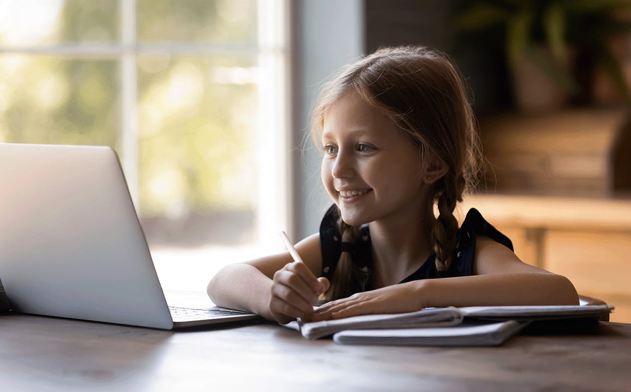 A young girl sits at a table, focused on her laptop