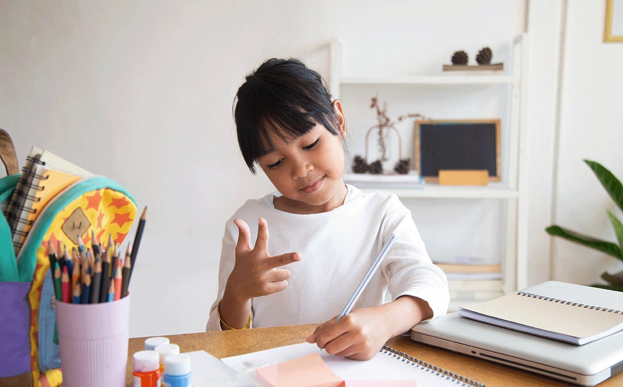 A young girl sits at a desk with a notebook open beside her, ready to take notes.