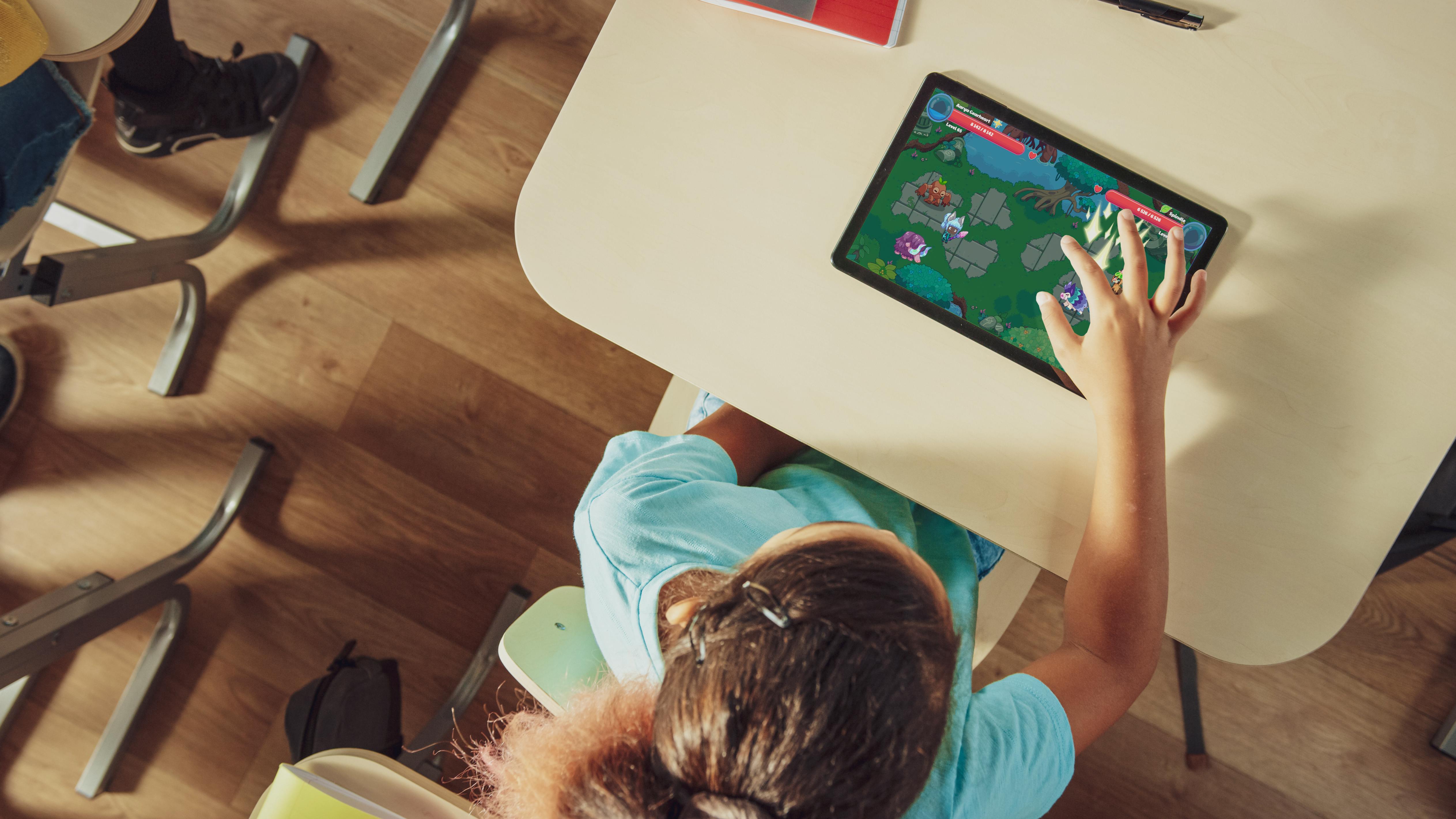 A young girl happily playing the Prodigy English game on a tablet in a classroom