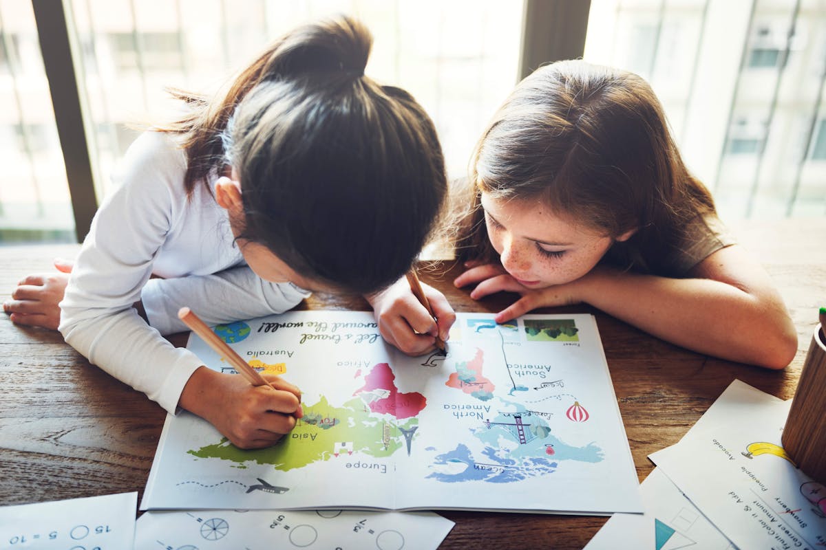 Two young girls happily drawing on a map with colorful markers
