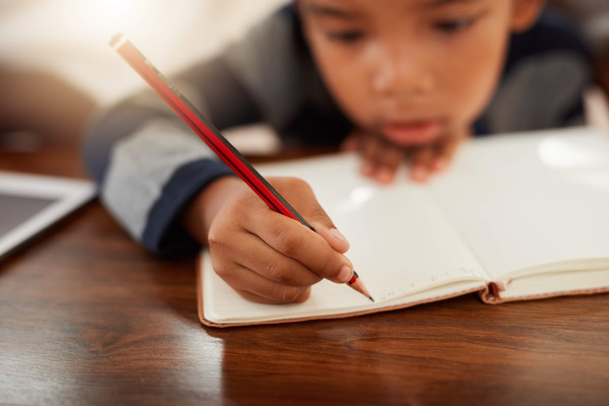 A young boy focused on writing in a notebook, expressing his thoughts and ideas