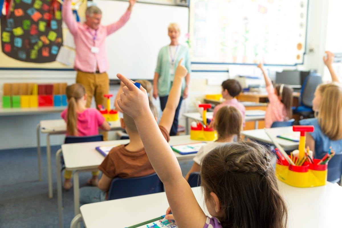 A classroom full of eager children raising their hands to participate in a lively discussion