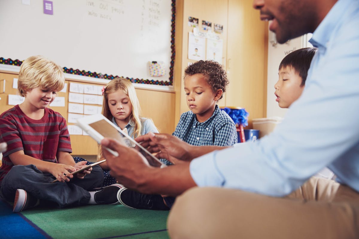 A teacher and kids sitting on floor in classroom, engaged in learning