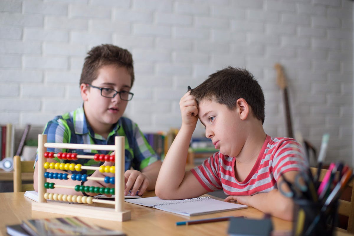 Two boys sitting with an abacus, looking confused. Kids facing math challenges