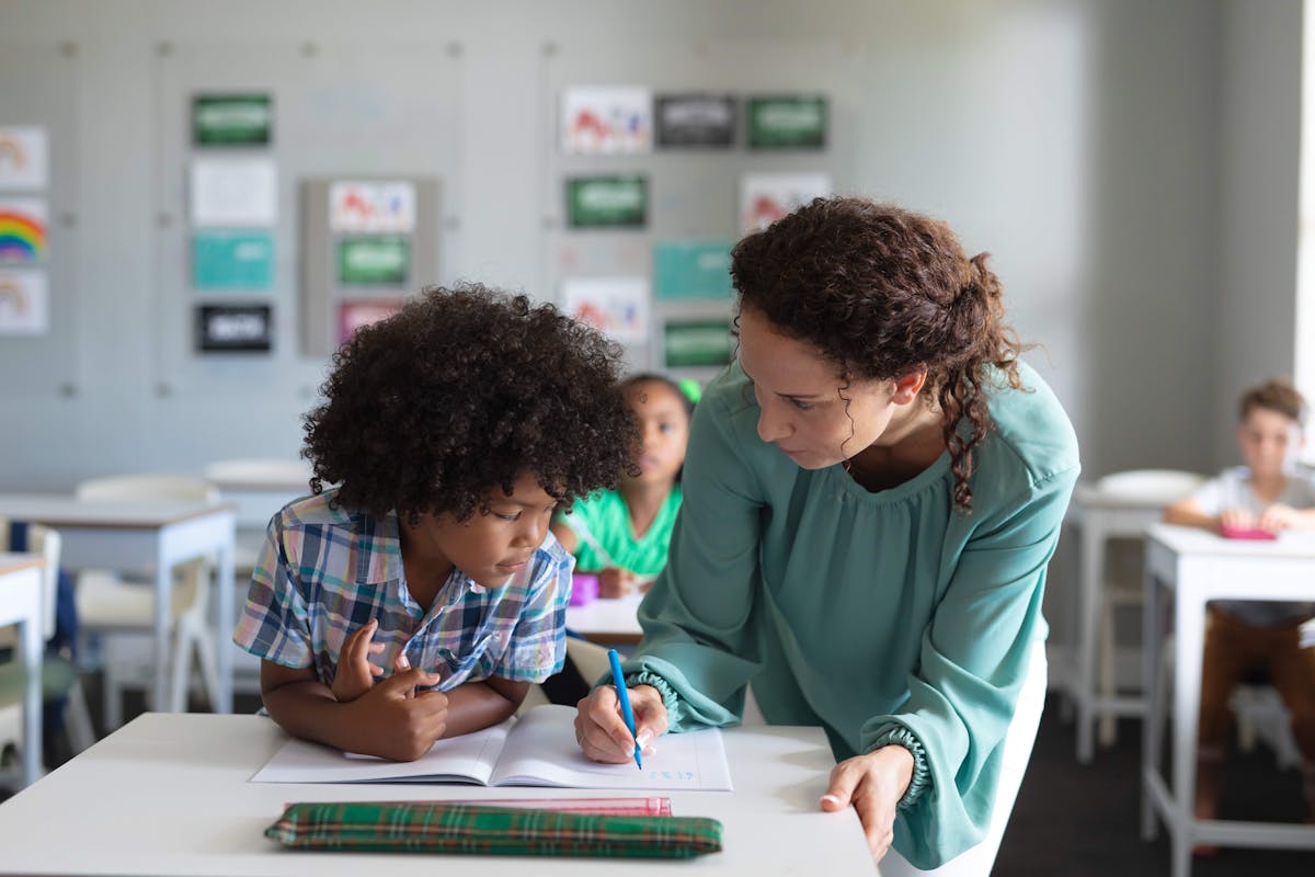 A teacher assisting a child with homework in a classroom, focusing on math