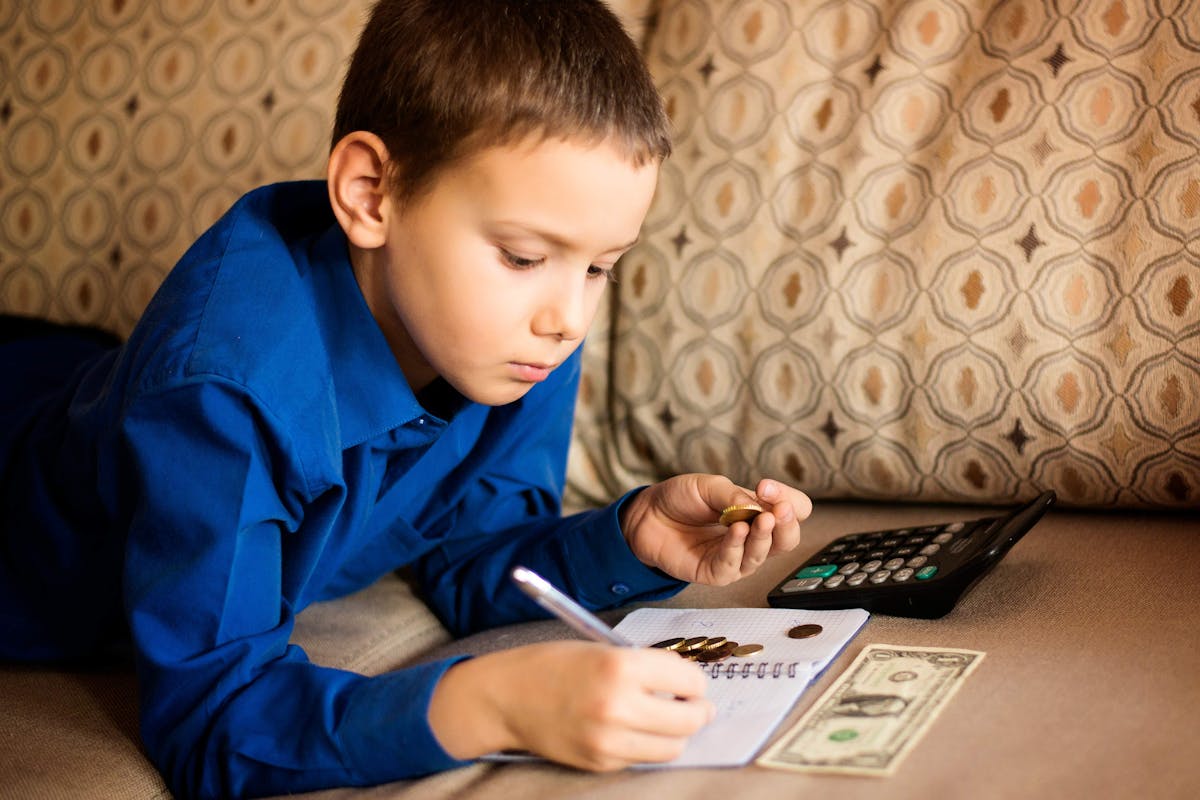 A young boy on a couch with a calculator and money, doing math with coins